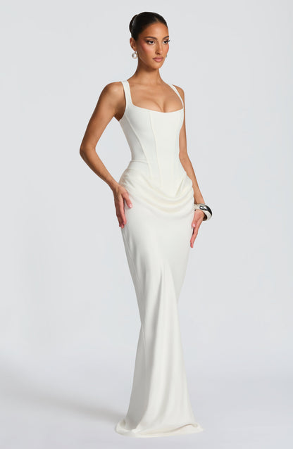 Angled view of the cream-white maxi dress, with hands resting on hips, showing the structured bodice and draped fabric. 9
