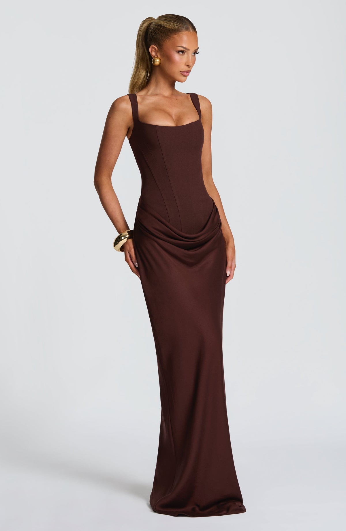 Three-quarter view of the brown corset maxi dress, with model looking to one side, showing the boned bodice and draped hip. 3