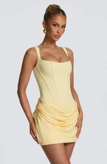 Three-quarter front view of the pale yellow dress, model's hand resting on the ruched skirt 24