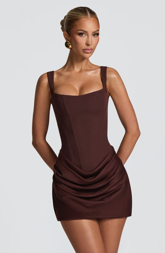 Model in the chocolate-brown corset-style mini dress, front close-up showing the square neckline, wide straps and draped skirt. 1