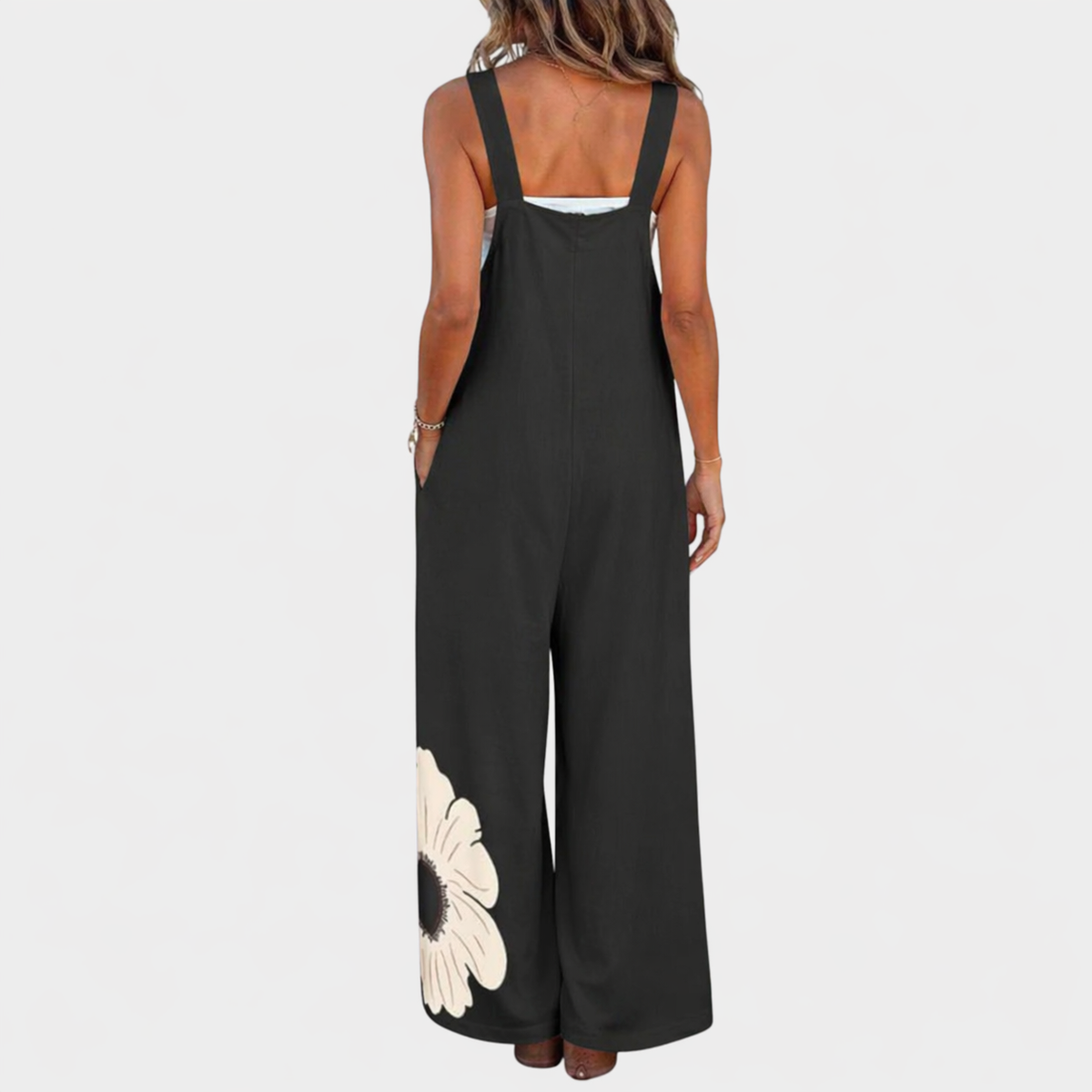 Back view of black dungarees on a model, with wide shoulder straps and a flower near the hem 3