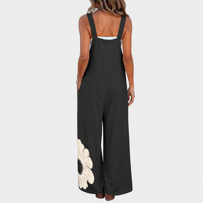 Back view of black dungarees on a model, with wide shoulder straps and a flower near the hem 3