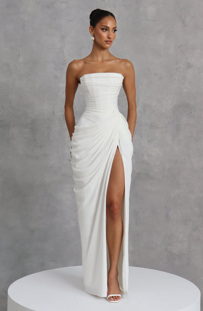 White strapless corset maxi dress styled with pearl earrings against a grey textured backdrop, model looking to the side. 13