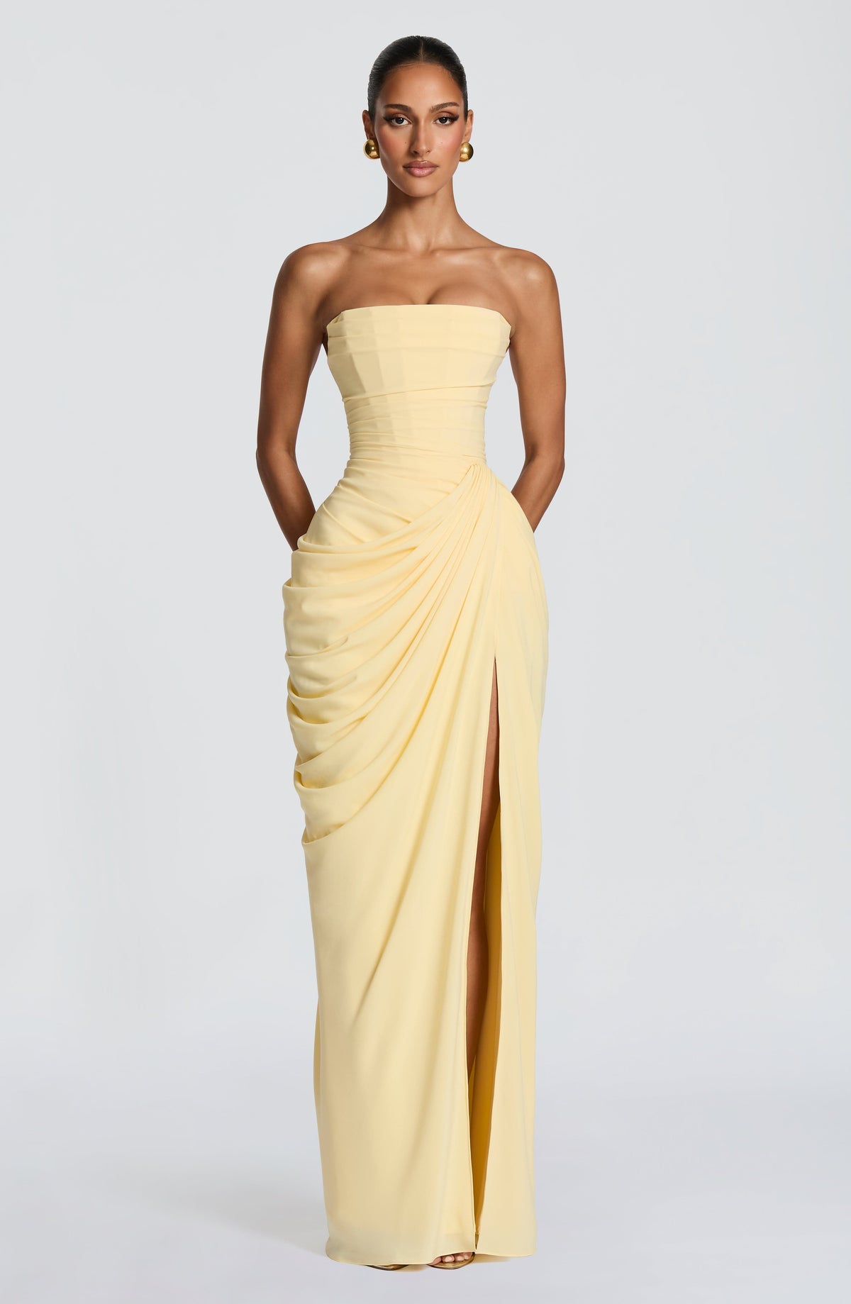 Full-length front view of the pale yellow strapless maxi dress, with arms behind and side drape gathered at the hip. 4