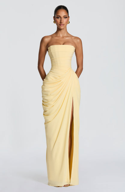 Full-length front view of the pale yellow strapless maxi dress, with arms behind and side drape gathered at the hip. 4