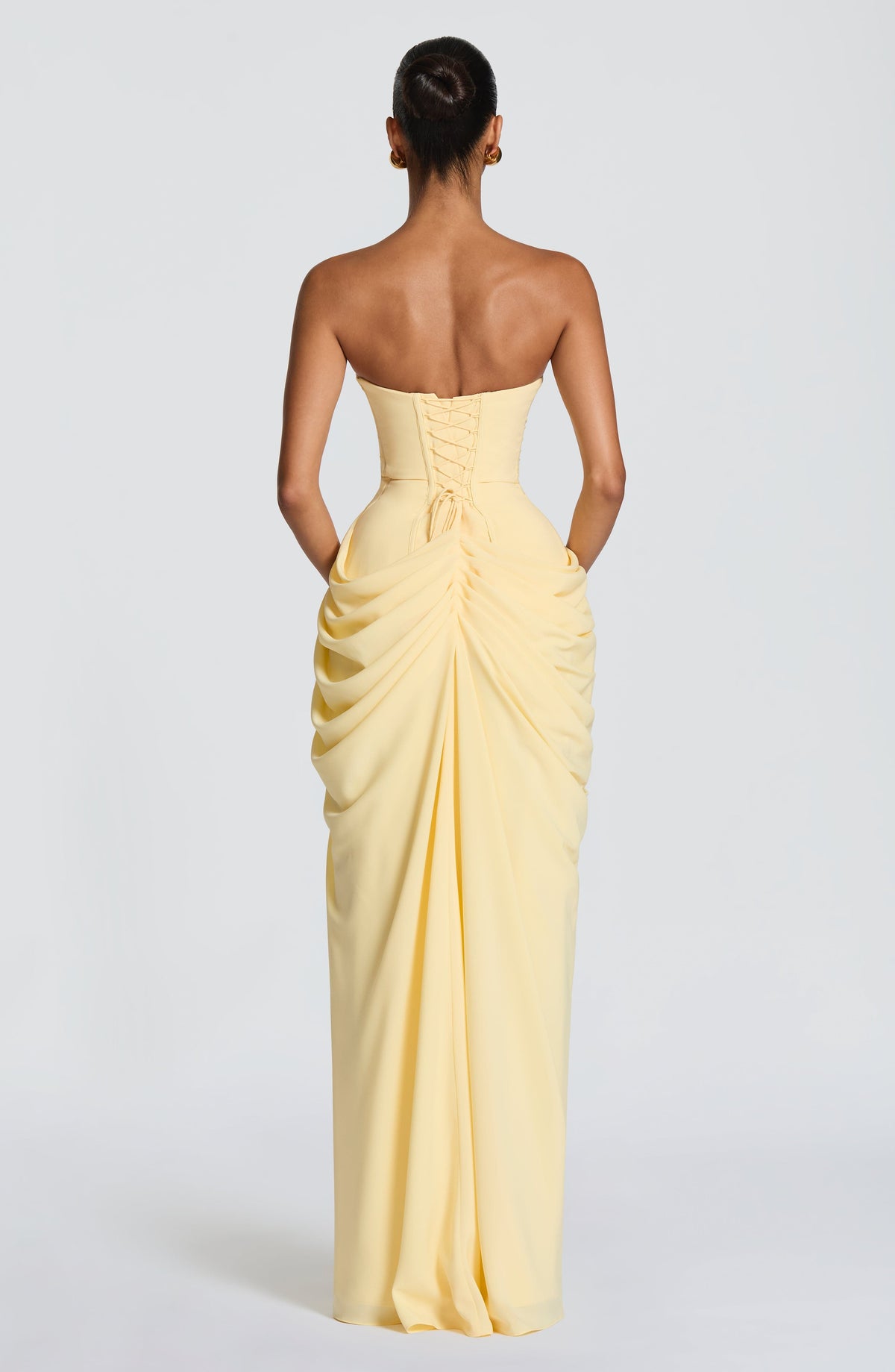 Back view of the pale yellow strapless dress showing the lace-up corset back and gathered, ruched drape down the skirt. 2