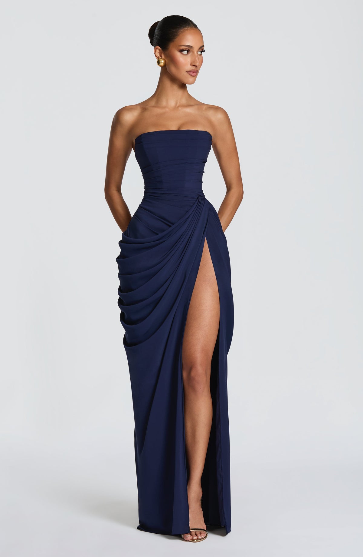 Navy strapless corset maxi dress with draped wrap skirt and high slit, styled with gold earrings and gold heeled sandals. 15