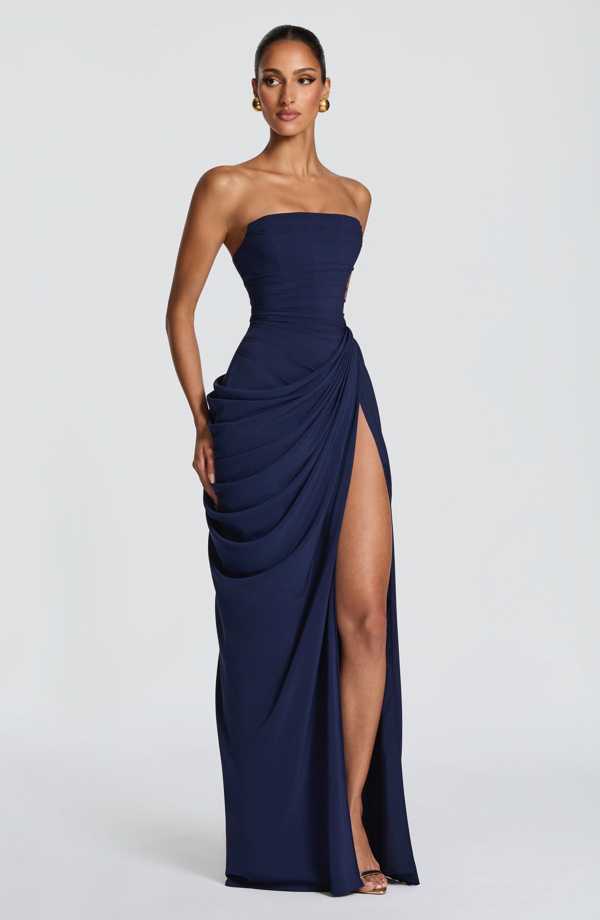 Angled front view of the navy strapless maxi dress, with one hand at the hip and the draped skirt open at the thigh slit. 17