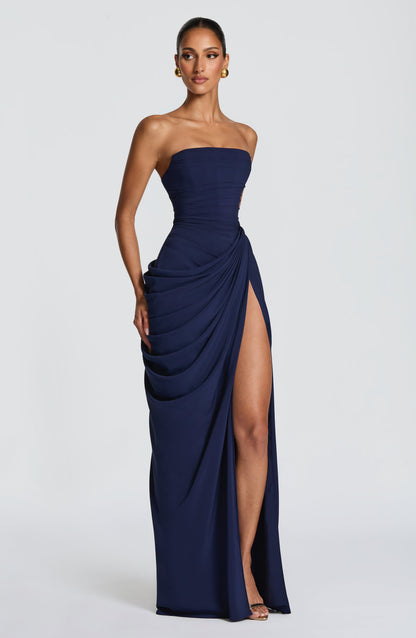 Angled front view of the navy strapless maxi dress, with one hand at the hip and the draped skirt open at the thigh slit. 17