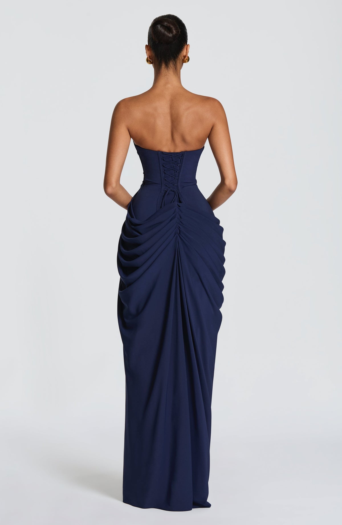Back view of the navy strapless dress showing the lace-up corset back and gathered, ruched drape down the skirt. 16