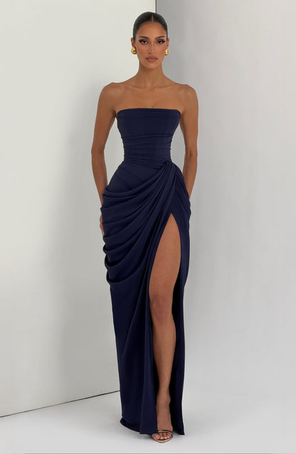 Navy strapless corset maxi dress worn against a light studio wall, front view showing the high slit and draped hip. 20