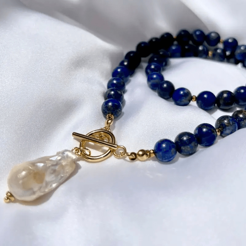 Close-up on white satin of the gold toggle clasp, blue beads and irregular baroque pearl 5