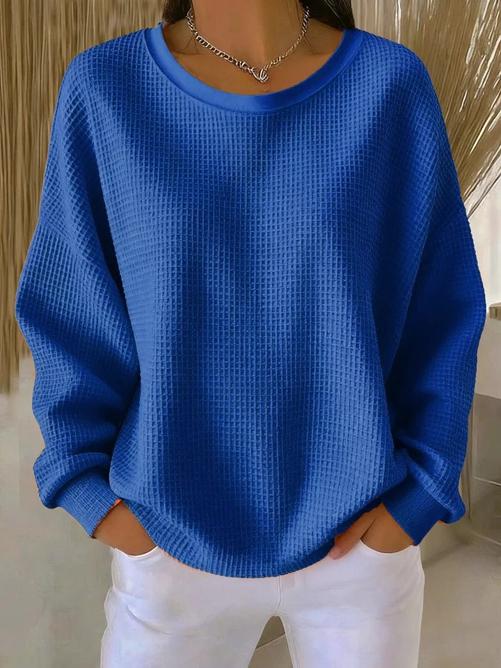 Model wearing the waffle-knit jumper in royal blue, with a crew neckline and loose sleeves, styled with white trousers. 5