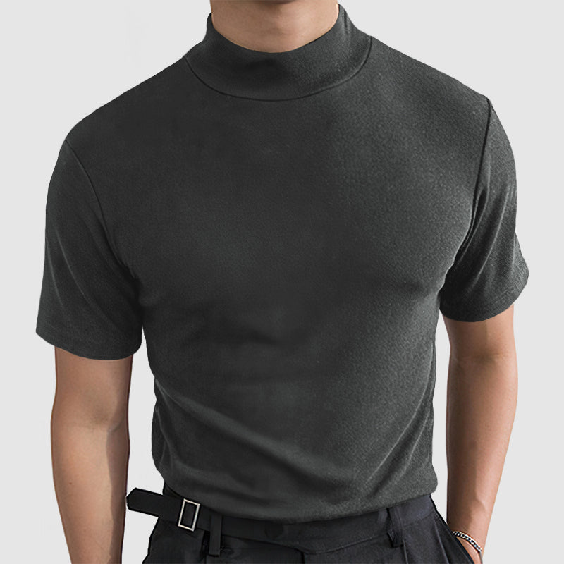 Front view on a model of the dark grey short-sleeved mock-neck tee, worn with dark trousers and a belt. 3