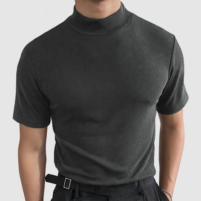 Front view on a model of the dark grey short-sleeved mock-neck tee, worn with dark trousers and a belt. 3