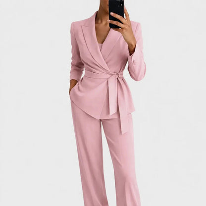 Model wearing the pink version of the wrap blazer with tie belt and matching straight-leg trousers, holding a phone. 4