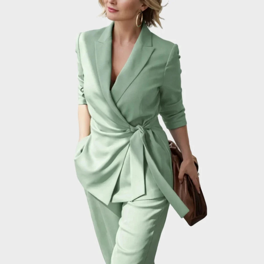 Close three-quarter view of the green wrap blazer knotted at the waist, worn with trousers and a brown handbag. 6
