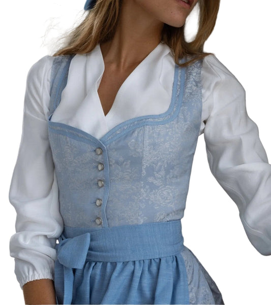 Model in a light blue floral jacquard dirndl bodice with pearl buttons, white blouse and blue apron, seen from the front at an angle. 1