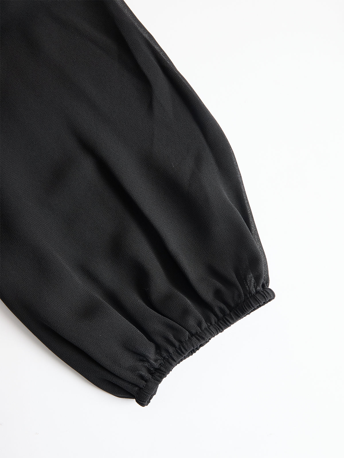 Close-up of a black sheer puff sleeve gathered into an elasticated cuff, laid flat on a white background. 4