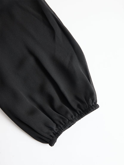 Close-up of a black sheer puff sleeve gathered into an elasticated cuff, laid flat on a white background. 4