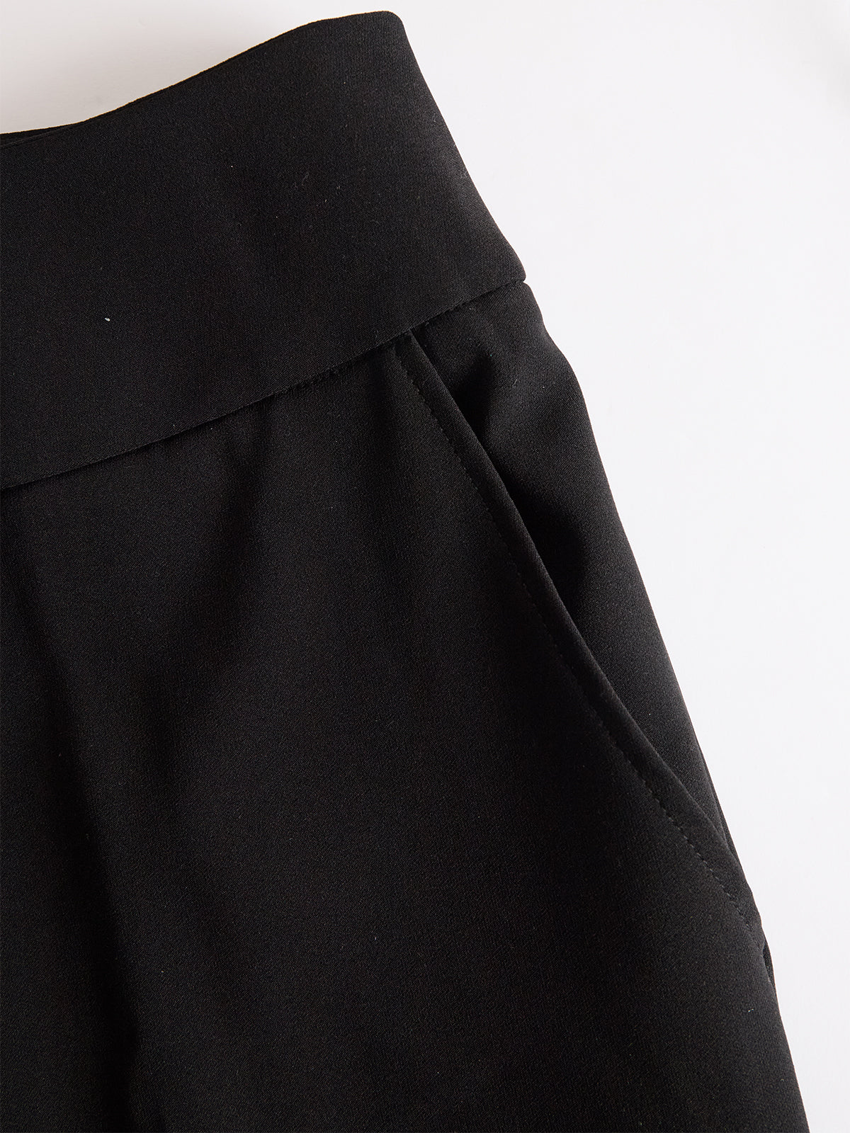 Close-up of the black trousers' wide waistband and side pocket, laid flat on a white background. 5
