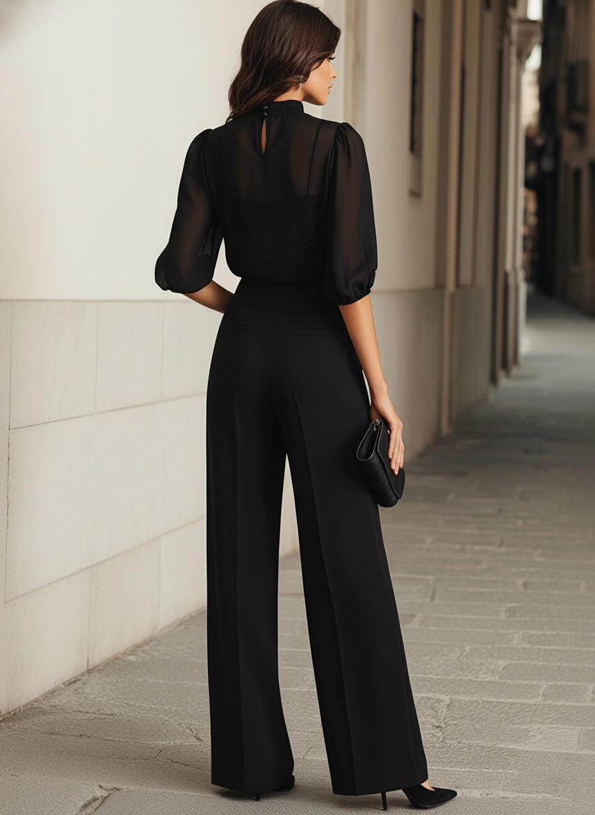 Back view of a model in the black set, showing the sheer top's keyhole button closure at the neck and the wide-leg trousers. 9