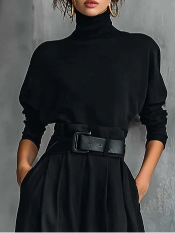 Close-up of the black high neck top, long sleeves and belted pleated waistband on a model 3