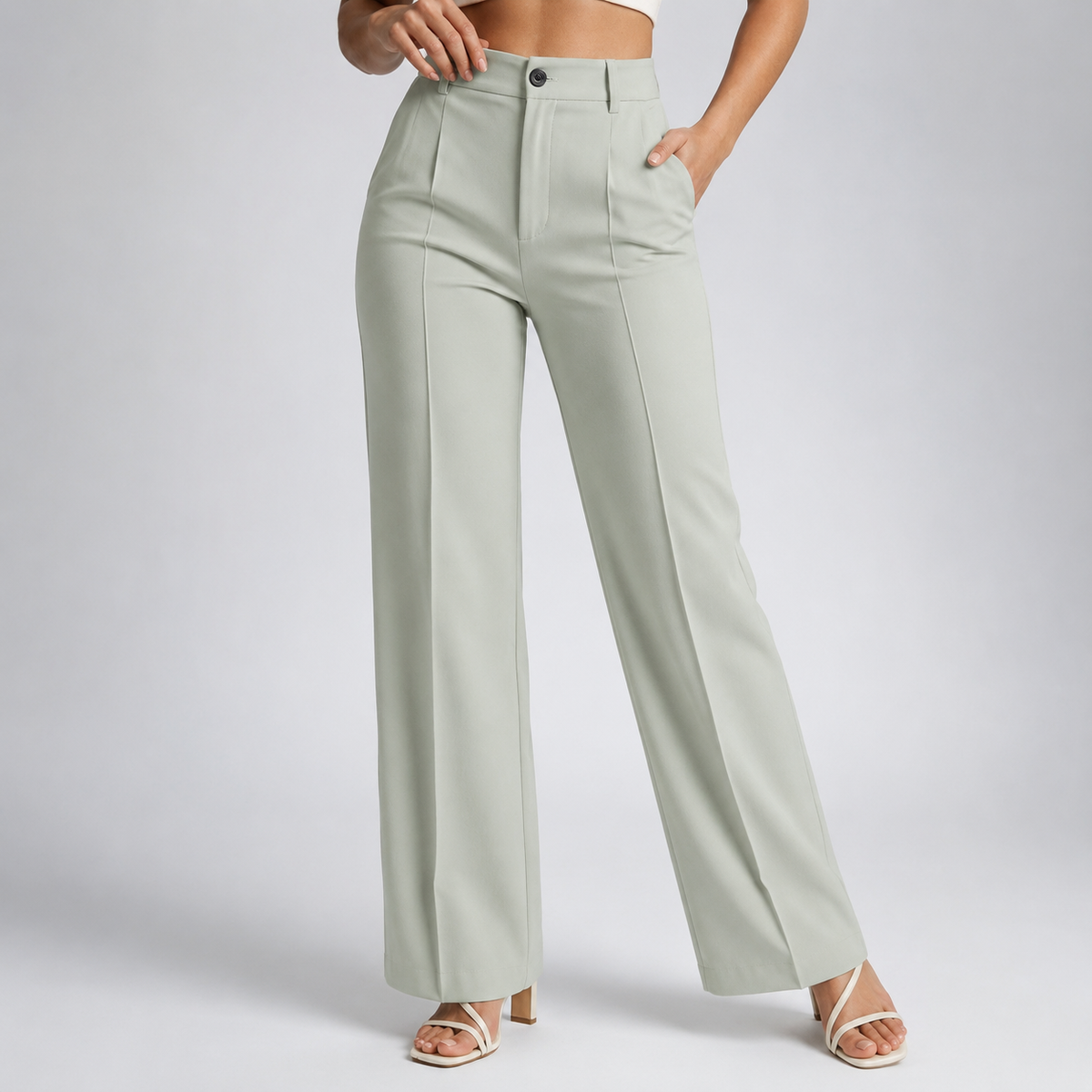 Model wearing pale sage-green high-waisted trousers with centre creases and one hand in the pocket, with cream strappy heels 23