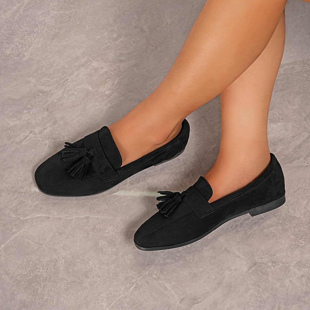 Black tasselled loafers worn by a seated model, shot from above on a grey stone floor 20