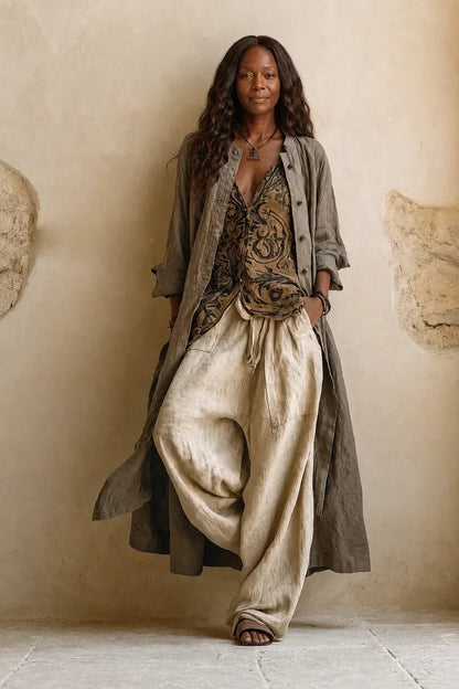 Model leaning on a plaster wall in the full set: long open cardigan, patterned top, wide trousers 1