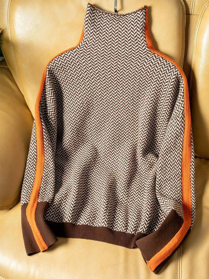 Brown and cream herringbone jumper laid flat on a tan leather sofa, showing the orange side stripes, brown hem and cuffs. 5