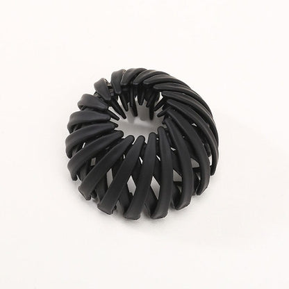 Single matte black spiral bird's-nest clip on a plain pale background, showing overlapping curved slats and inner prongs. 14