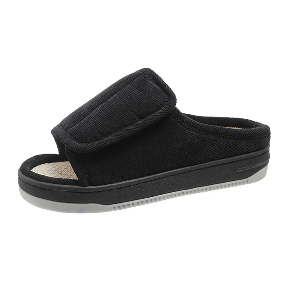 Single black corduroy open-toe slipper with a wide adjustable strap, woven insole and a grey tread sole, seen from the side. 1