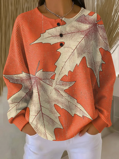 Orange waffle knit henley jumper printed with large cream maple leaves, worn with white trousers 14