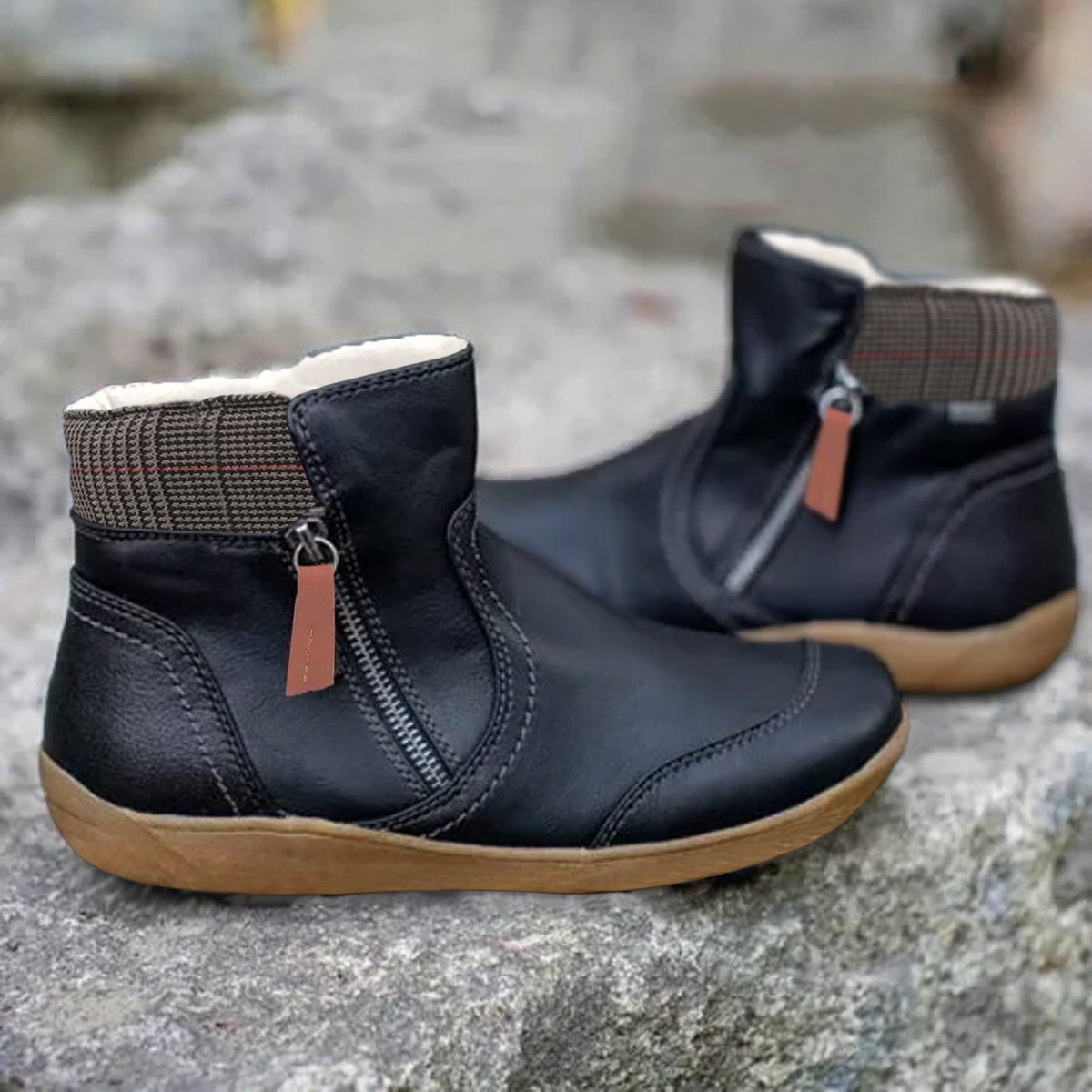 Black version of the ankle boots with side zip and orange-brown pull tab, houndstooth collar and tan sole, on a stone surface. 2