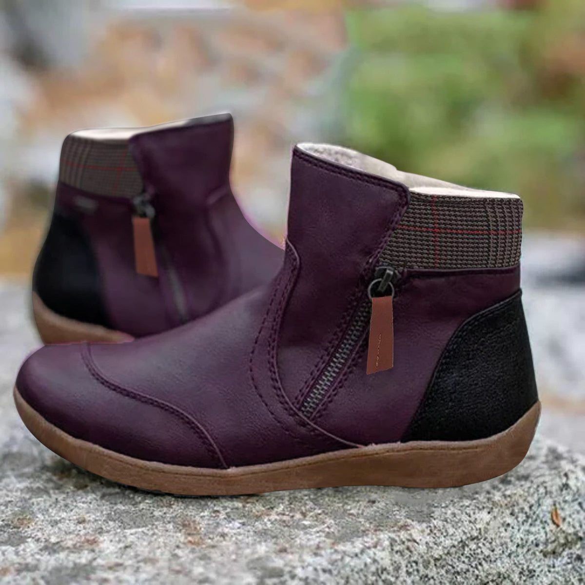 Deep purple version of the ankle boots with side zip, checked fabric collar, black heel panel and brown sole, on a rock. 4