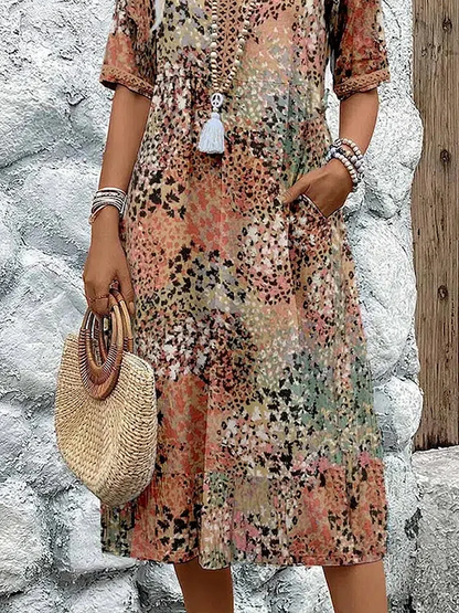 Close-up of the lower half in the earthy print, showing the side pocket, tiered skirt hem and a round straw handbag. 7