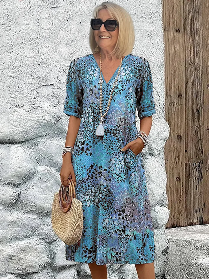 Same V-neck midi dress with half sleeves in a blue speckled print, worn by the model with a beaded tassel necklace. 2