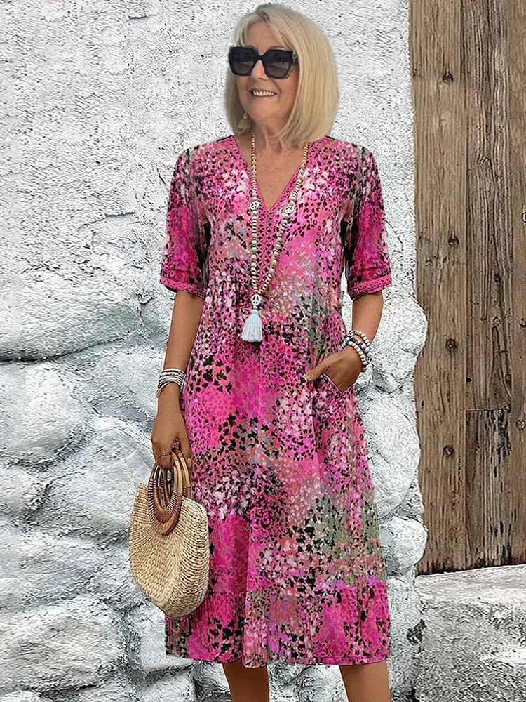 Model wears the dress in a bright pink speckled print, one hand in the pocket, carrying a woven straw handbag. 3