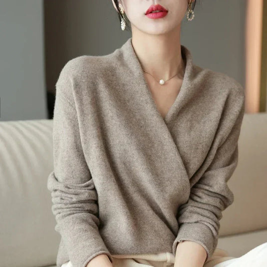 Model in taupe wrap-front knit jumper with pearl earrings and necklace, seated on a cream sofa 1