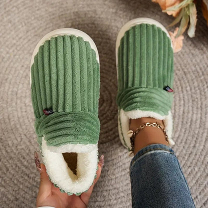 Green ribbed slippers viewed from above, one held in a hand and one worn, on a woven rug. 13