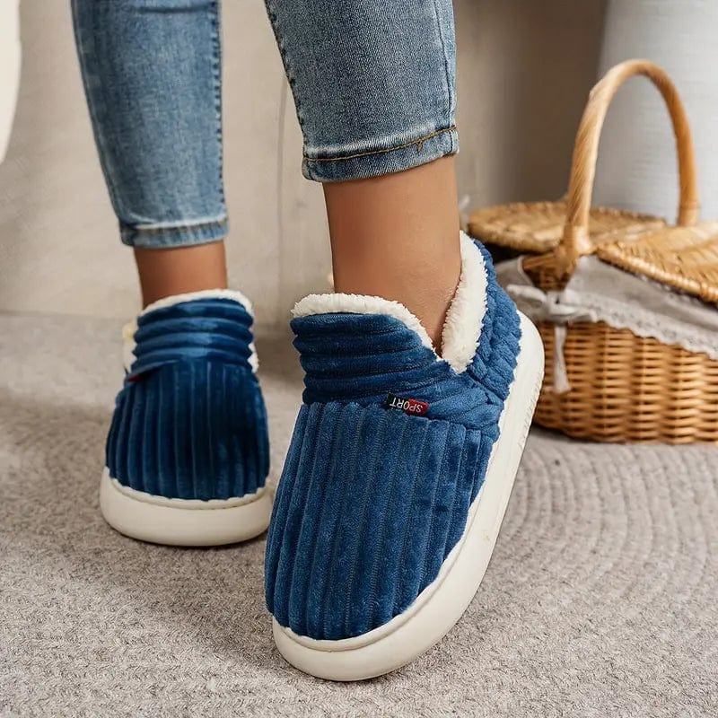 Blue ribbed slippers worn by a model in jeans, standing on a grey rug beside a wicker basket. 5