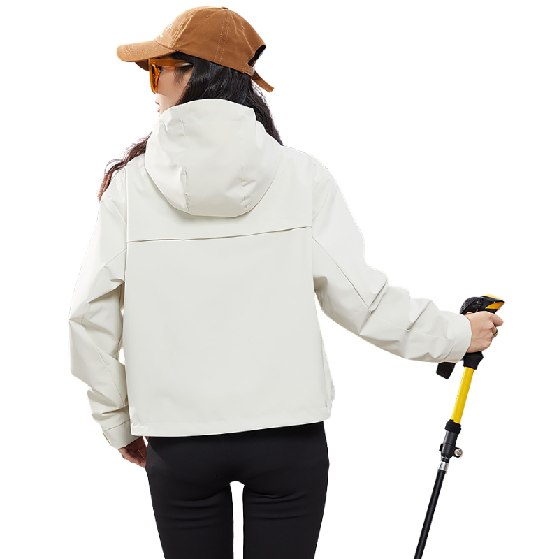 Back view of the cream jacket on a model holding a trekking pole, showing the hood and the yoke seam across the shoulders. 5