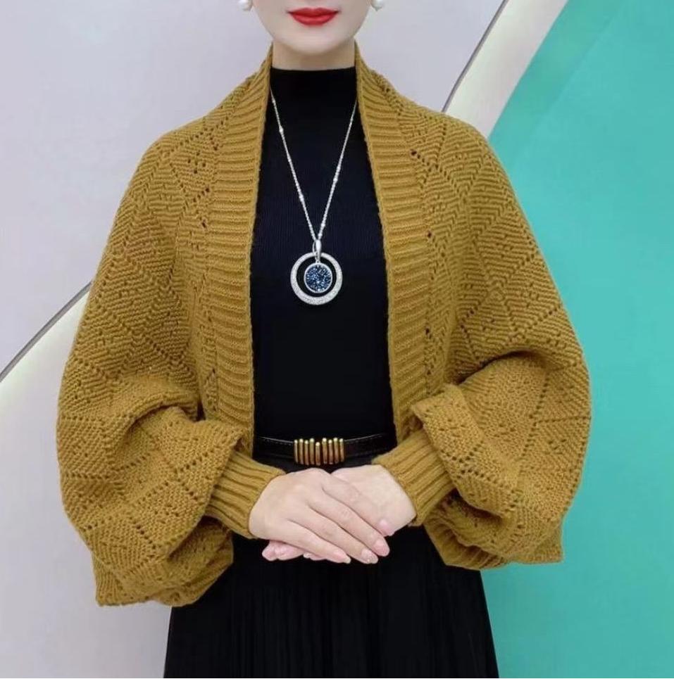 Model wearing the open knit shawl cardigan in mustard yellow over black, with a teal backdrop 1