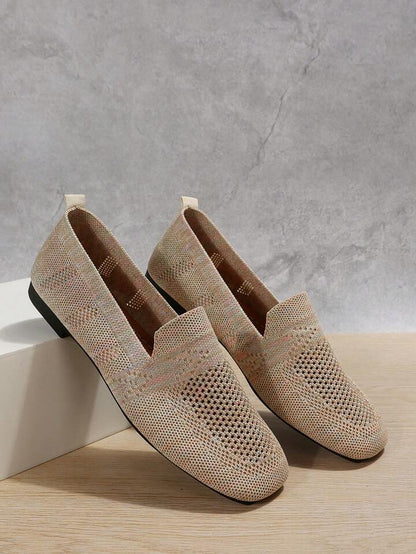Pair of beige speckled knit slip-ons with perforated toes and a heel pull tab, leaning against a white block. 7