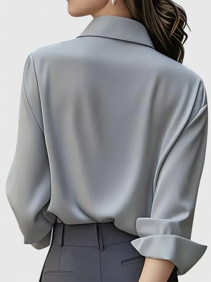 Back view of the grey blouse on a model, showing the smooth back, turned-up cuff and collar, worn with dark grey trousers. 8