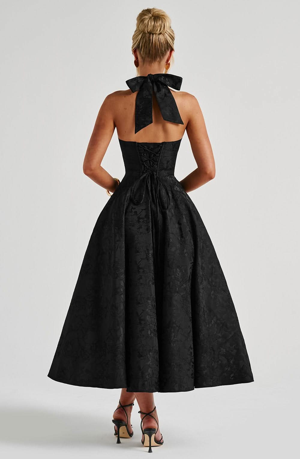 Back view of the black halter dress, showing the tied neck bow, open back, corset lacing and full skirt. 14