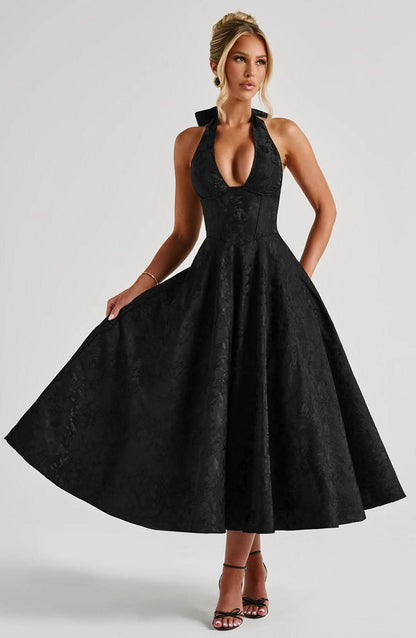 Black halter midi dress on a model who gently holds out the full skirt, front view with plunging neckline and corset bodice. 13