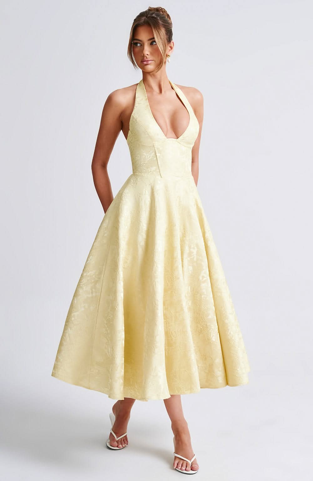 Pale yellow version of the halter midi dress worn by a model, front view with deep neckline and full tonal floral skirt. 4