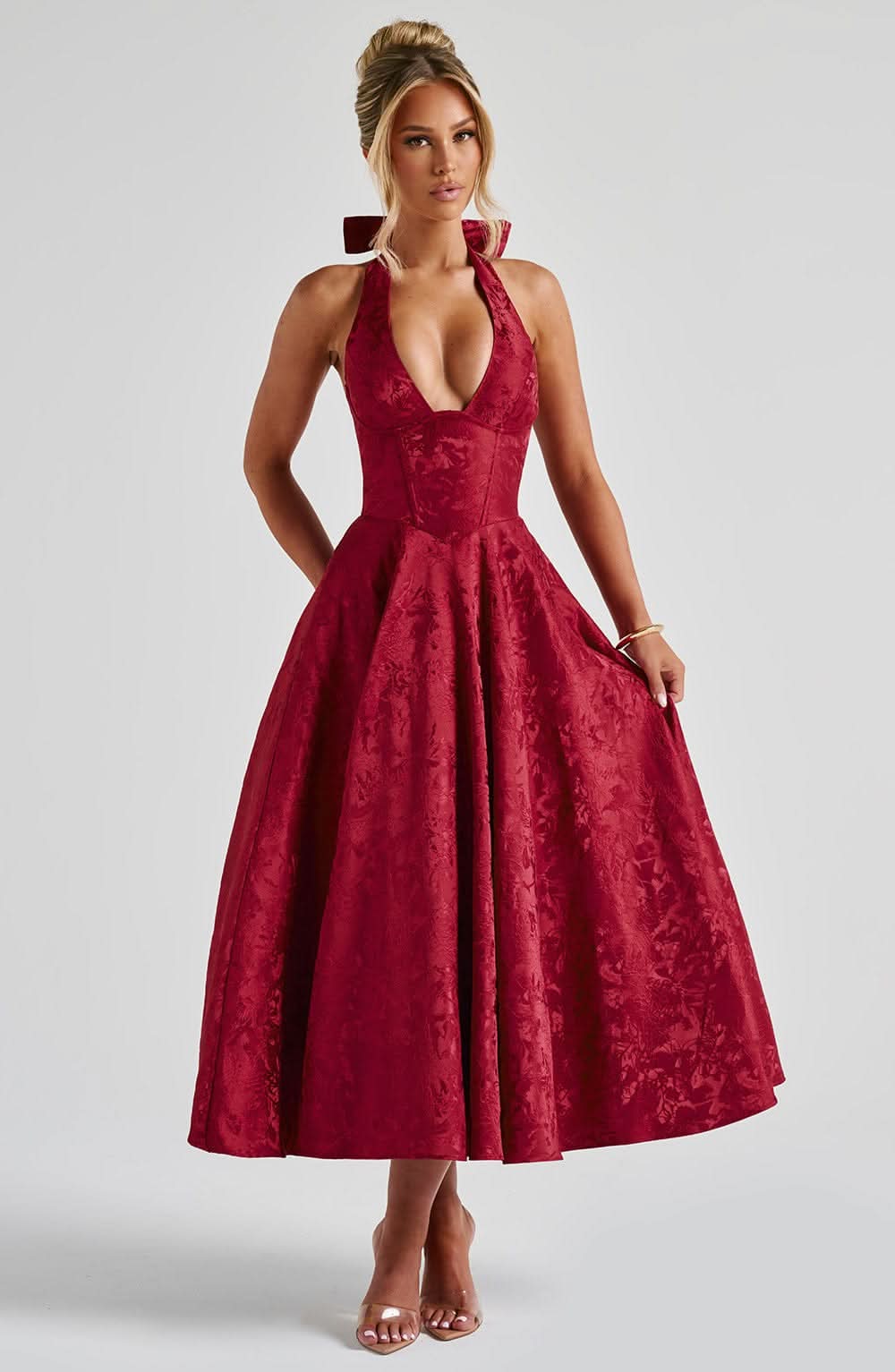 Deep red halter midi dress on a model, front view with plunging neckline, corset bodice and full floral jacquard skirt. 10